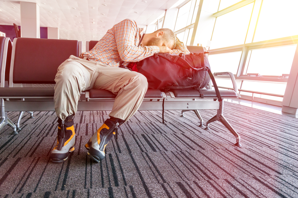 student sleeping in an airport wondering how to find a cheap plane ticket for his return flight