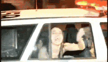 A woman blowing a kiss out of the back window of a police car
