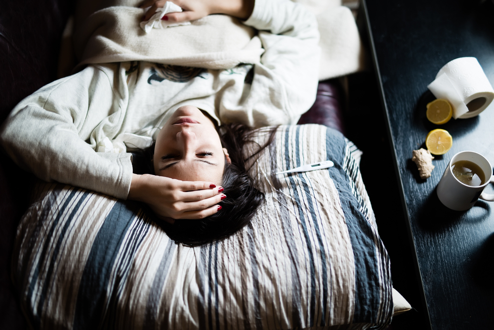 A girl lies sick in bed and wonders why she didn't get a flu shot in college.