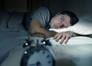 A man dealing with insomnia in college lays in his bed with his eyes wide open.