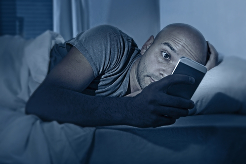 A man checks his phone in bed; the light from a phone can lead to insomnia in college.