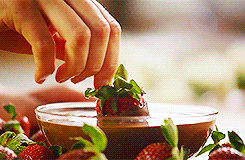 A person dips a strawberry into melted chocolate; this could be a good snack during finals week.