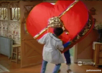 A boy carries a massive heart-shaped box of Valentine's Day chocolates into the house.