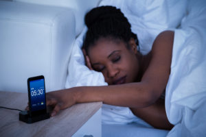 A sleeping girl presses the snooze button on her phone.